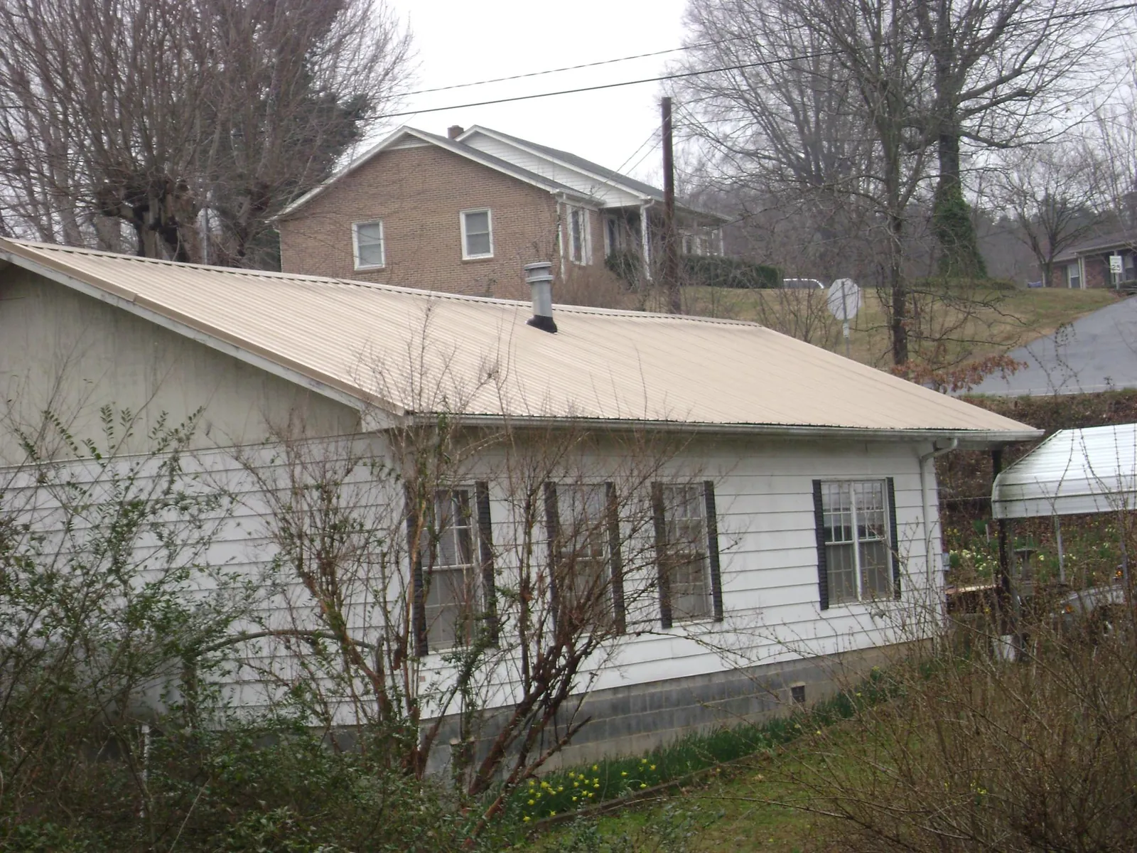 Tan metal roof on a white sided house set into a hillside — Commercial Roofing by Roofing Brothers in Oak Park
